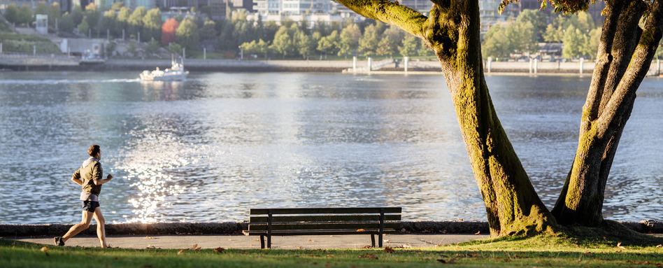A person runs through a park with a shimmering bay in the background.