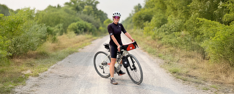 Carole sits on her bike on a gravel trail with trees and bushes on either side. Carole sits on her bike on a gravel trail with trees and bushes on either side.