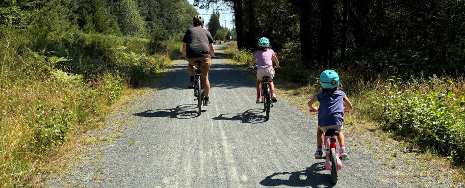 Two children with their parent bike along a gravel trail.