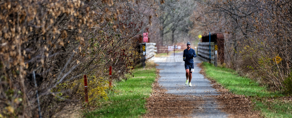 A person runs on a paved trail with recently fallen autumn leaves around them. A person runs on a paved trail with recently fallen autumn leaves around them.