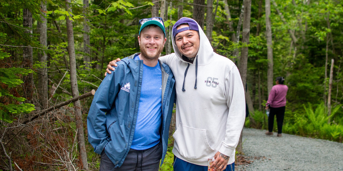 Two people pose for a photo with a forest behind them. Two people pose for a photo with a forest behind them.