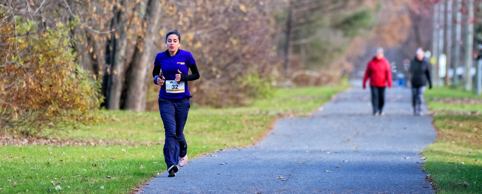 A person runs on a paved trail with recently fallen autumn leaves around them. A person runs on a paved trail with recently fallen autumn leaves around them.