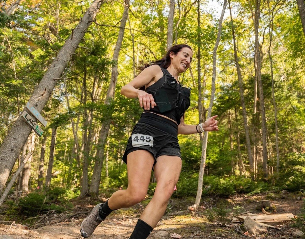 Chrissy runs on a trail surrounded by trees during a marathon.